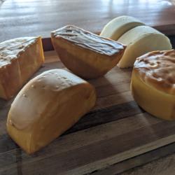 Half rounds of cheese displayed on a wood cutting board some with wax covering some without.
